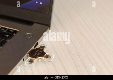 A contemporary silver laptop with a glowing blue screen and a multi-port USB drive inserted, placed on a white wooden desk for seamless file managemen Stock Photo