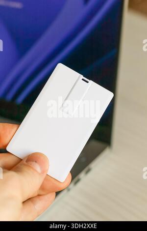 Close view of a hand showing a blank white slim USB storage device in card format near a computer. Stock Photo