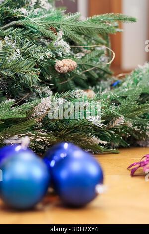 Lush artificial fir branches dusted with faux snow and adorned with pinecones, paired with hanging blue glass baubles and purple floral accents on a w Stock Photo