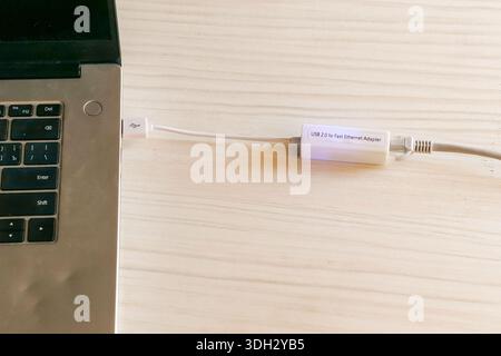 Detailed view of a white USB to Gigabit Ethernet adapter with attached gray network cable on light table Stock Photo