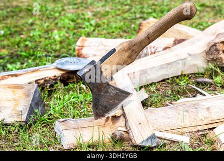 Axe for chopping firewood and chopped firewood lying on the grass in summer Stock Photo