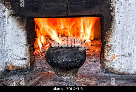 Brick oven with cast iron pot and burning firewood at the village house, close up Stock Photo