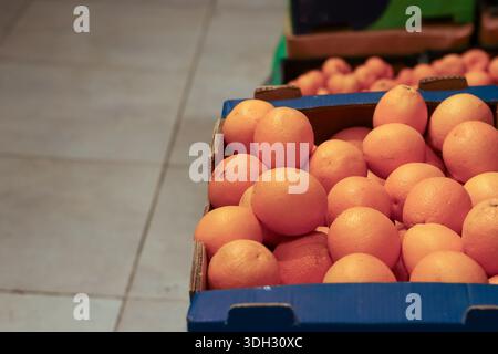 Close-up of ripe orange fruits piled in blue cardboard boxes on grocery store floor display. Stock Photo