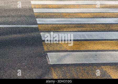 Faded yellow and white zebra crossing lines on road surface with shadows and texture details Stock Photo