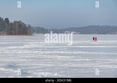 A couple enjoying winter walking on a frozen lake surrounded by snowy trees on a bright day Stock Photo