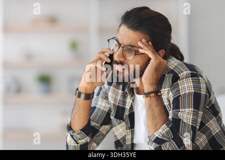 Upset middle-eastern guy having phone conversation, home interior Stock Photo