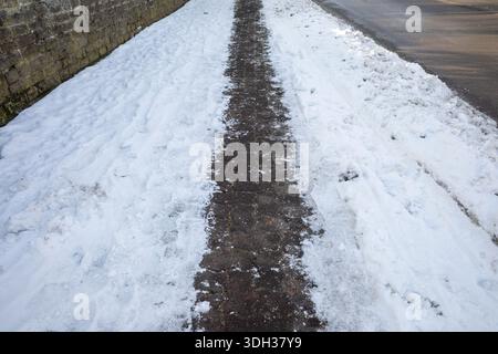snowy sidewalk in winter with a narrow walking path Stock Photo