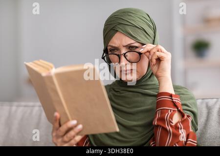 Senior Muslim Woman Having Poor Eyesight Reading Book At Home Stock Photo