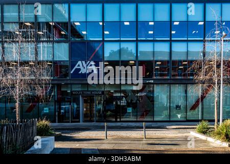The modern glass facade of Wolfe Tone House in Dublin, featuring the prominent AXA logo, reflected city life on a crisp, bright day. Stock Photo