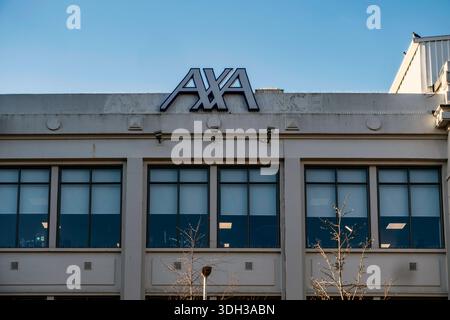 The prominent blue and white AXA Insurance logo is mounted atop a corporate office building in Dublin against a clear, bright blue sky. Stock Photo