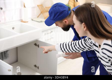 Young woman pointing at pipes to plumber in kitchen Stock Photo