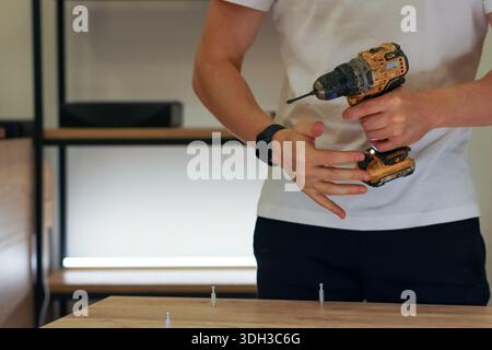 Individual using fingers to guide screw while holding drill in workshop environment Stock Photo