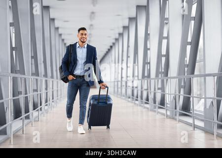 Portrait of young middle eastern man walking in airport terminal with luggage Stock Photo