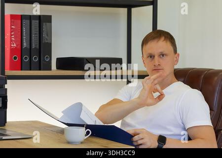 Male employee in quiet contemplation shushing or thinking with documents and coffee on desk Stock Photo