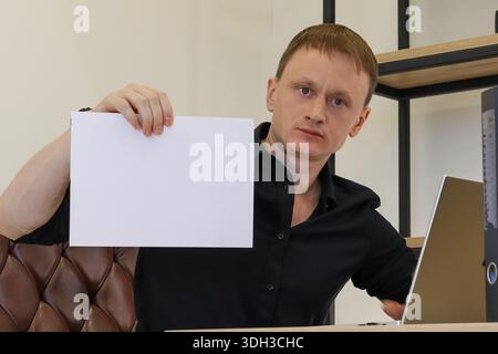 Young worker lifting white empty paper above head in office setting, with serious expression Stock Photo