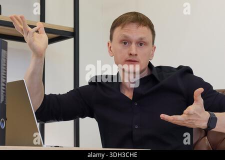 Young adult male at desk in office, spreading hands in gesture of explanation or questioning. Stock Photo