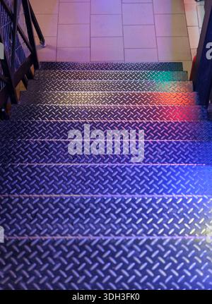 Top-down view of steel staircase steps with raised diamond plate pattern, multicolored light reflections in blue, red and green tones Stock Photo