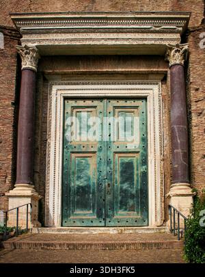 Weathered green double doors of the Temple of Romulus framed by carved stone and red marble columns open to a historic temple entrance, evoking ancien Stock Photo