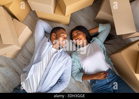 Loving black family with carton boxes around, lying on floor and having rest on moving day, top view Stock Photo