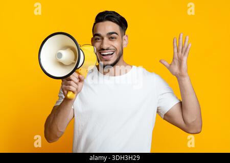 Excited arab guy speaking loud, using megaphone on yellow Stock Photo