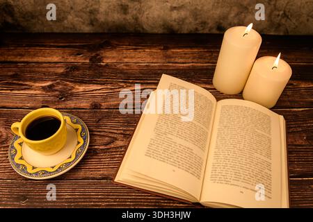 Top view cozy still life: open book, coffee cup and two lit candles on rustic wooden table. Plenty of copy space for text. Stock Photo