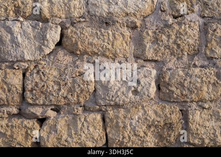 Close up texture of an old limestone stone wall with rough blocks, visible cracks, and aged mortar. Authentic historic masonry surface. Stock Photo