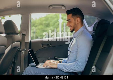 Young arab man CEO working at car backseat, using laptop Stock Photo