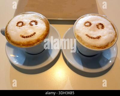 Top view of two Cappuccino Coffee cups with cocoa and cinnamon funny faces. Stock Photo