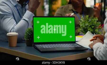 Green screen laptop used by programmers in startup office leveraging AI tech to gain competitive edge. Management doing meeting to discuss training deep learning models using mockup notebook, camera B Stock Photo