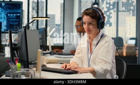 Developer listening music while working in AI startup training predictive models for language processing tasks. Tech expert wearing audio headphones uses technical expertise for IT tasks, camera B Stock Photo