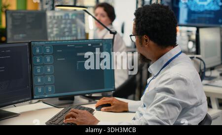 Programmer in office using AI LLM chatbot to get help optimizing systems performance metrics. IT worker in tech agency utilizing generative AI LLM assistant for faster software development, camera B Stock Photo