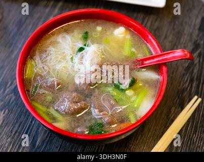 Deep clay bowl is filled with hot noodle soup and veal fillet. Stock Photo