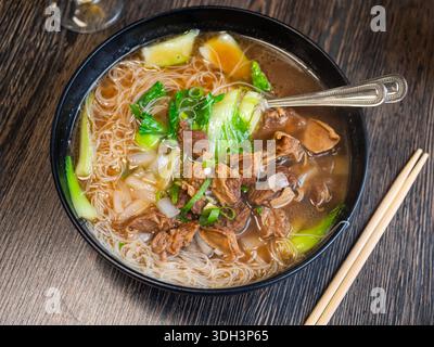 Deep clay bowl is filled with hot noodle soup and veal fillet. Stock Photo