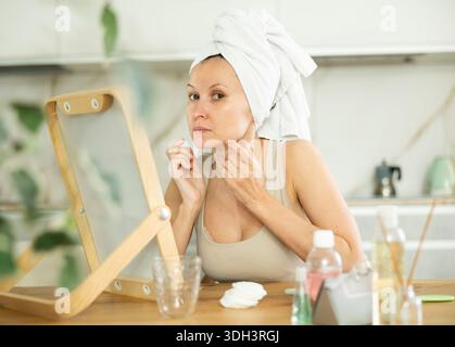 Middle-aged woman examining her facial skin looking in the mirror put on the table Stock Photo