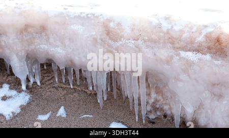 Icicles Forming on Sandy Beach During Cold Winter Season Stock Photo