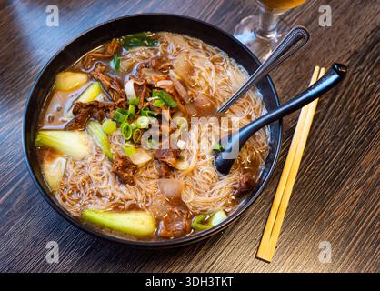 Deep clay bowl is filled with hot noodle soup and veal fillet. Stock Photo