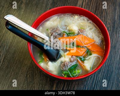 Deep clay bowl is filled with hot noodle soup and veal fillet. Stock Photo