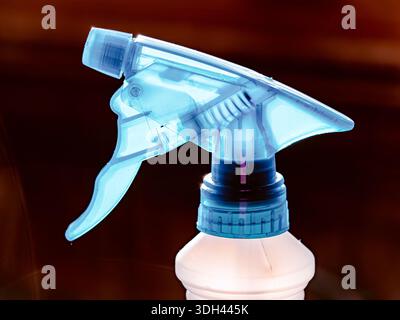 Close-up of a blue plastic trigger spray bottle nozzle on a white cleaning product container against a dark background, symbolizing household cleaning Stock Photo