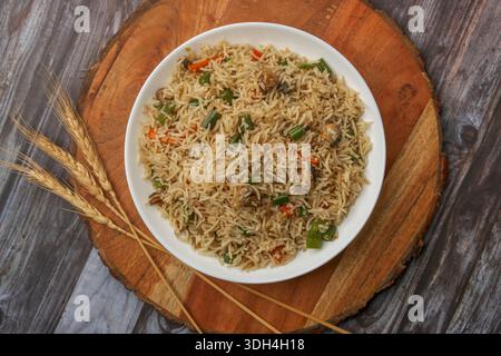 A bowl of rice with vegetables and meat on a wooden table. The rice is cooked and looks delicious. Stock Photo