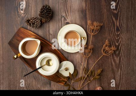 A wooden table with a tea set on it, including a teapot, a cup, and a saucer. The table is set with a variety of tea cups and a pitcher. Indian masala Stock Photo