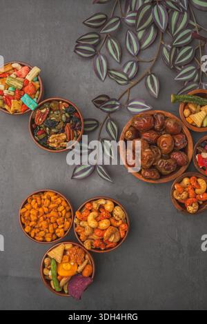 A variety of nuts and dried fruits are displayed in bowls on a grey background. The bowls are arranged in a way that creates a sense of abundance and Stock Photo