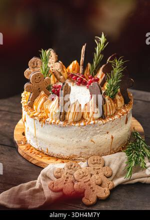 A festive spiced layer cake decorated with gingerbread man cookies, rosemary, and red currants, featuring a golden caramel drip and creamy white frost. Stock Photo