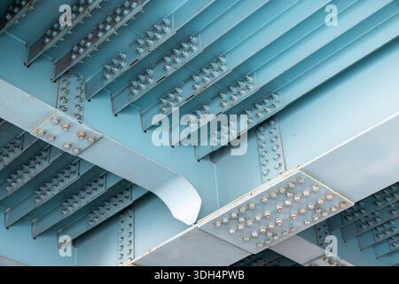 A dramatic view of the underside of a teal-painted steel bridge, featuring riveted girders, repeating ribs, and structural spans. Ideal for architectu Stock Photo