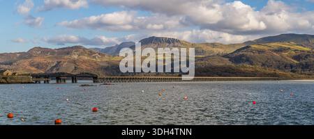 Barmouth, Wales, March 06, 2024: Wide panoramic view across the Mawddach Estuary, with the historic railway bridge and dramatic mountains under a clou Stock Photo