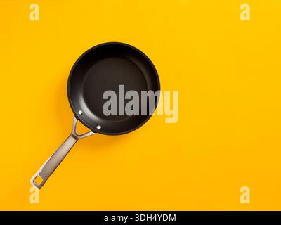 Empty black frying pan with a stainless steel handle on a vibrant yellow kitchen background, shot from top view Stock Photo