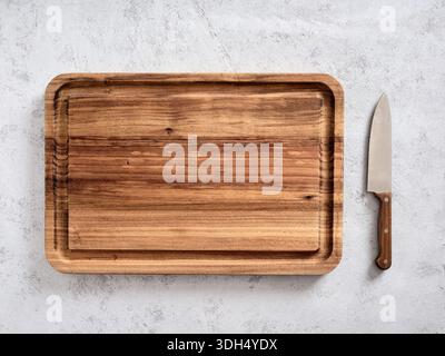 Empty wooden cutting board with a chef knife next to it, resting on a light concrete background for cooking preparation Stock Photo