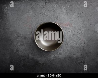 Empty black ceramic bowl centered on a dark grey concrete table with rough texture. Minimalist and top view Stock Photo