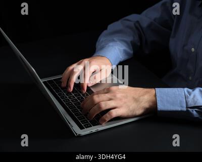 Man's hands typing on a laptop keyboard, working, learning, or communicating on a computer with a dark background Stock Photo