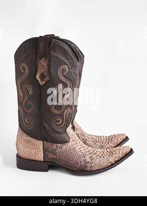 Side view of Western style cowboy boots handcrafted from genuine dark brown leather and light beige snakeskin on white background. Stock Photo