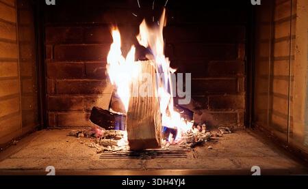 Close-up of burning wood logs in a brick fireplace with vibrant orange flames. Warm, cozy atmosphere for winter home comfort and heating concepts. Stock Photo